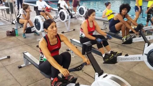 women working out on rows of indoor rowing machines in a gym