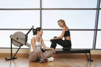 women talking next to rowing machine