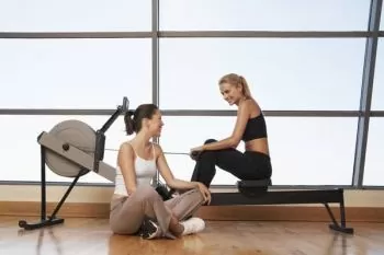 two young women talking at rowing machine in health club