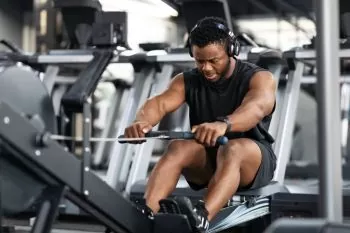 man rowing at gym with headphones