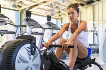 a lady in white and blue outfit working out on a rowing machine at a gym 