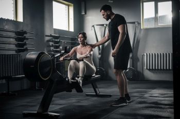 trainer at gym show lady how a rowing will change her body shape & fitness