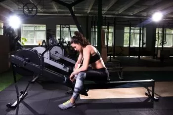 a woman sitting or resting on the rail of a rowing machine 