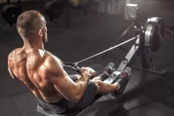 back of a man with huge muscles using an indoor rowing machine