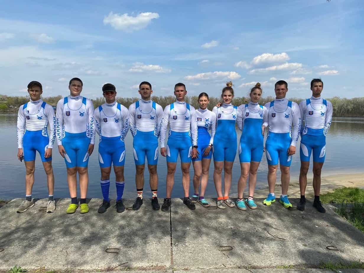 male and female rowers wearing their team uniform and standing on the shoreline of a lake