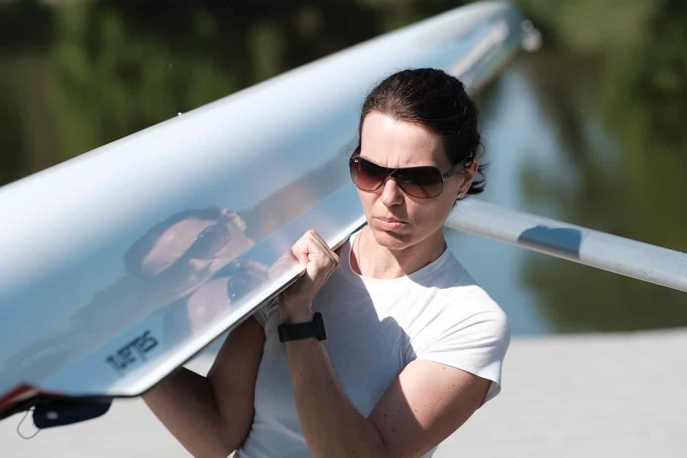 Lady in a white shirt carrying a rowing shell
