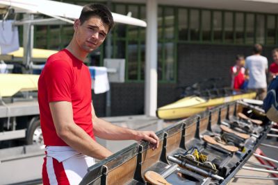 A man wearing red and white outfit standing beside a rowing boat