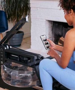 a lady using her phone while sitting on a CityRow Go rowing machine 