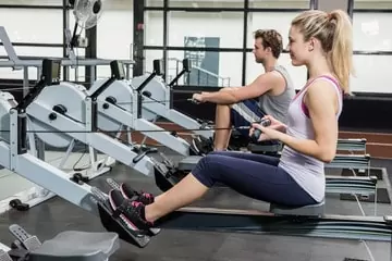 Man and lady at the gym rowing on an indoor erg