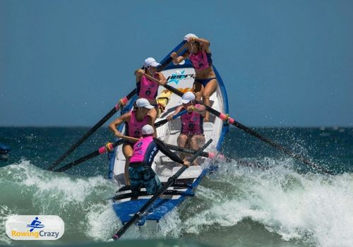 women rowers paddling the surf boat through the waves