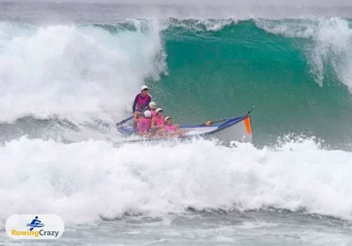 a women's surf boat rowing team taking on a huge wave